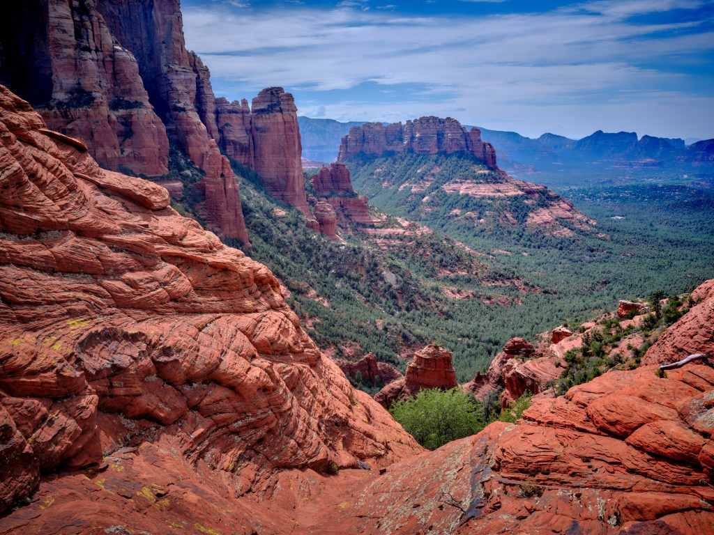 Red slickrock and canyon walls overlooking a green valley near Devils Bridge in Sedona.