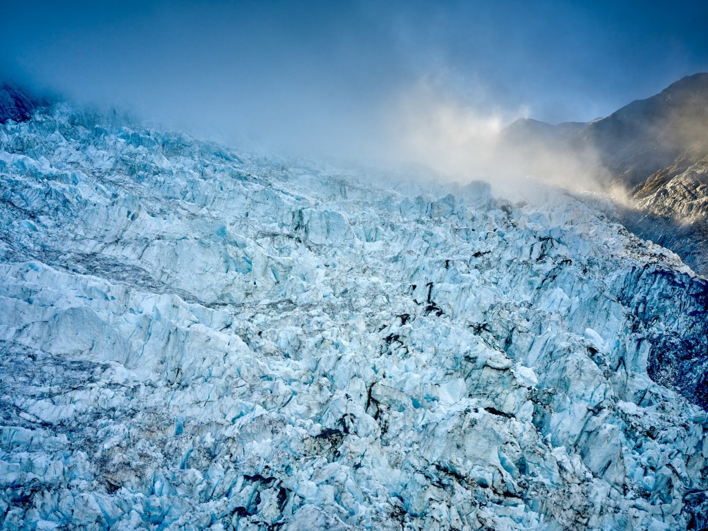 New Zealand 38 Rough serrated ice ridges spread across the glacier surface below cold blue mountain light.