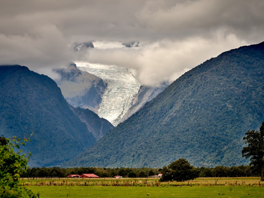 New Zealand 73 A distant glacier appears between steep shadowed mountains under a stormy sky.
