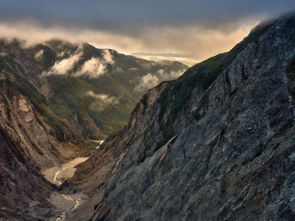 New Zealand 56 A helicopter view looks down a rugged valley carved by ice beneath dramatic mountain light.