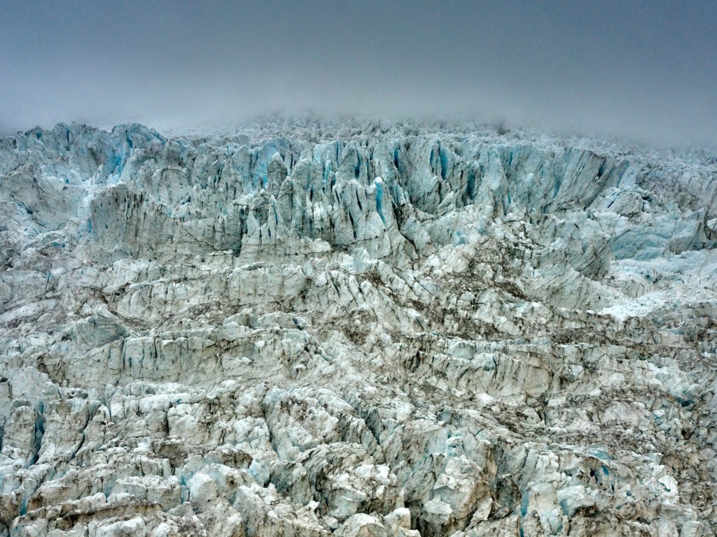 New Zealand 33 Jagged blue white ice ridges fill the frame below a low gray cloud ceiling.