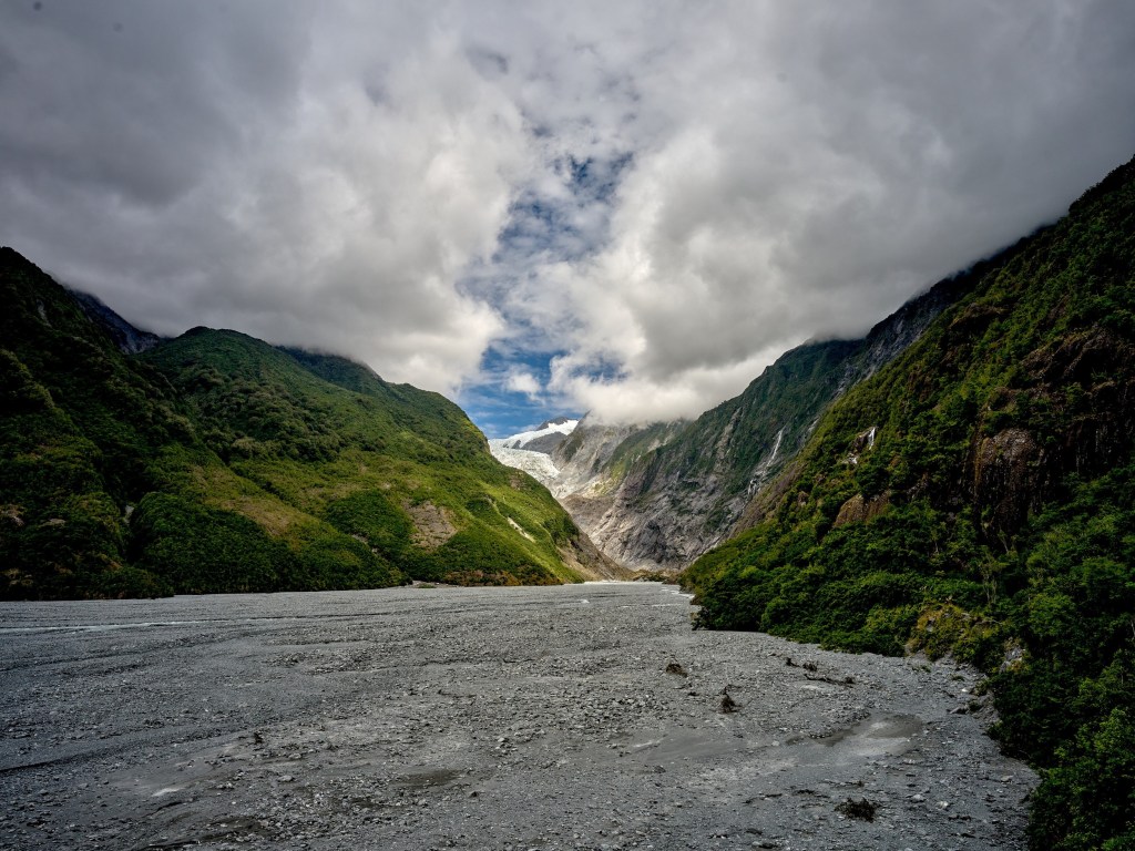 New Zealand 71 A broad gray moraine stretches into a steep green valley beneath heavy mountain clouds.