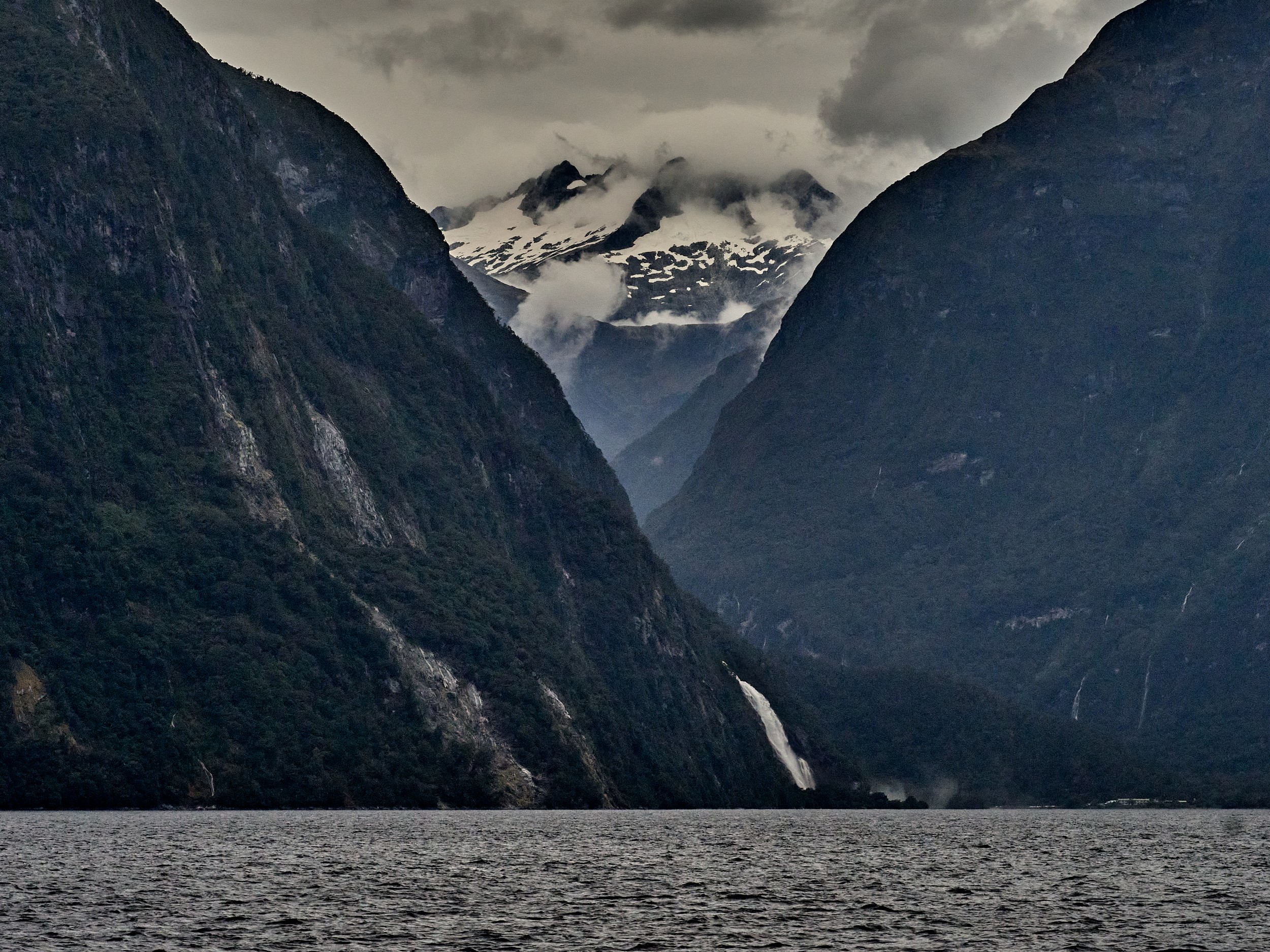 Milford Sound 14 Dark fjord walls frame the inner end of Milford Sound as waterfalls appear beneath low gray clouds.
