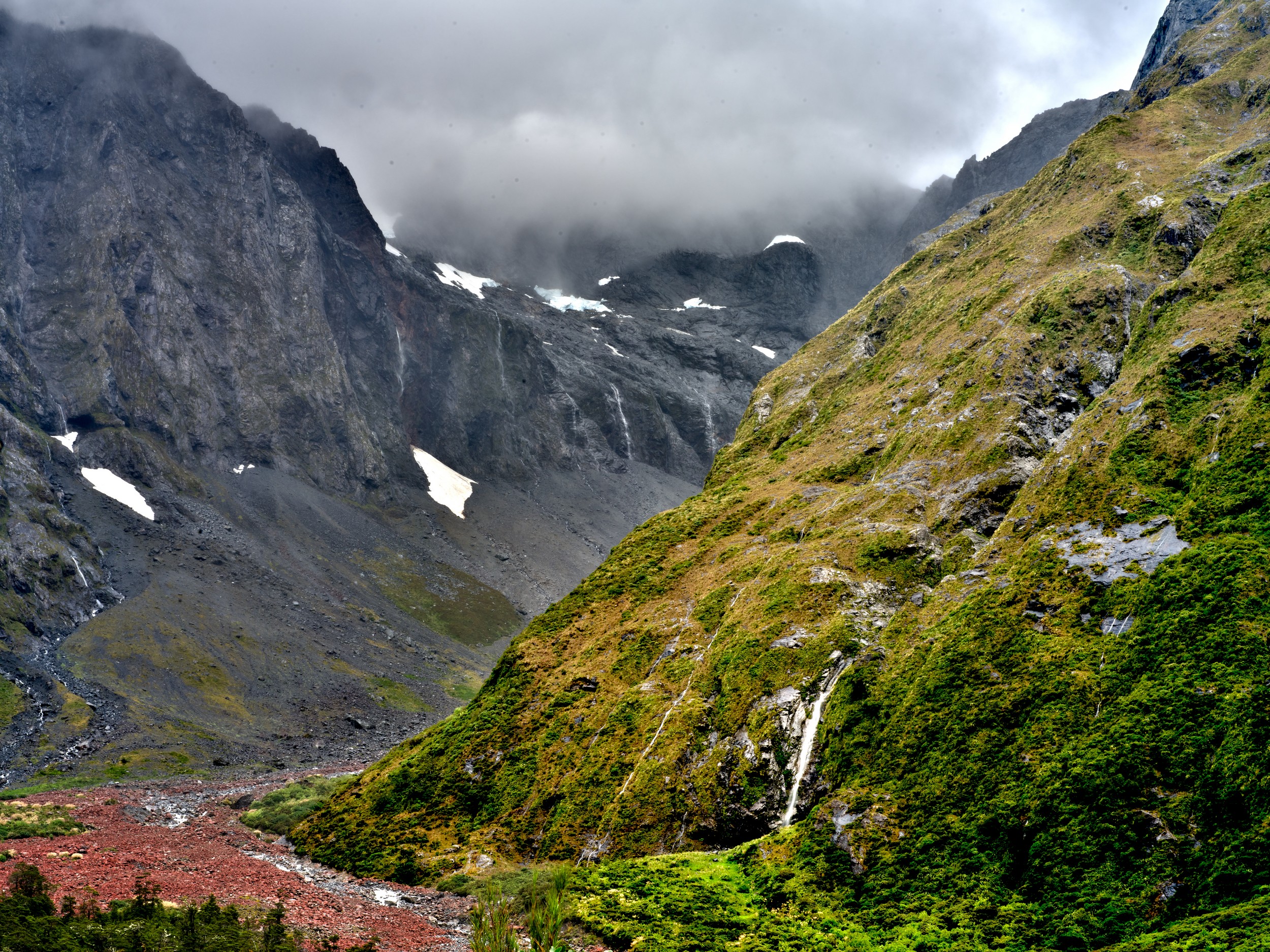Milford Sound 13 A glacier-carved valley narrows between dark mountains, with cloud bands and waterfalls above the Milford Sound road.