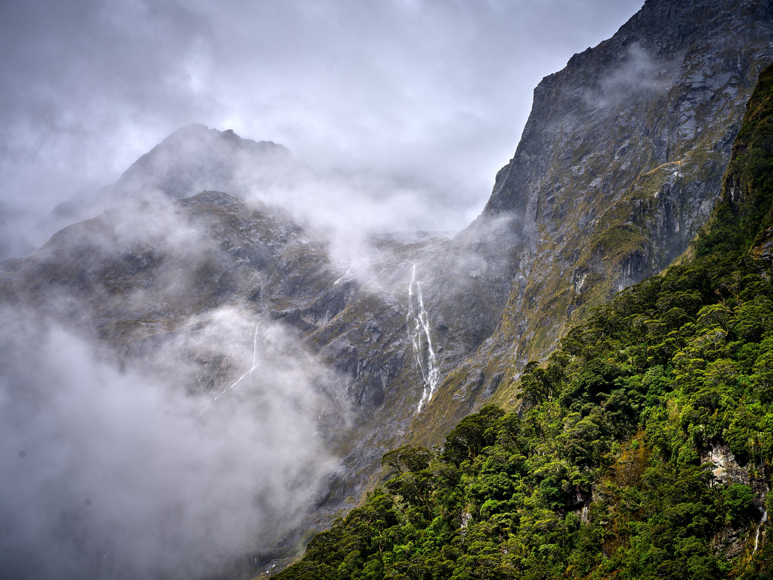 Milford Sound 22 Rain clouds drift through steep green cliffs as fresh waterfalls streak down the mountainsides near Milford Sound.
