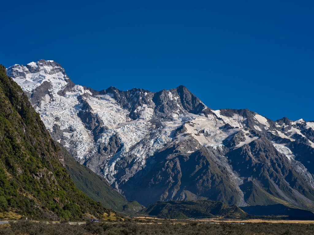 New Zealand 60 Steep gray cliffs and bright snowfields dominate a clear alpine view in the national park.