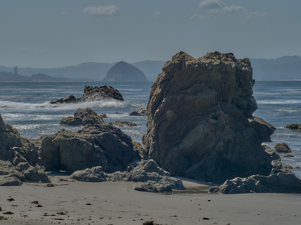 Sunlit sea stacks rise from the sand as distant headlands fade across the bay.