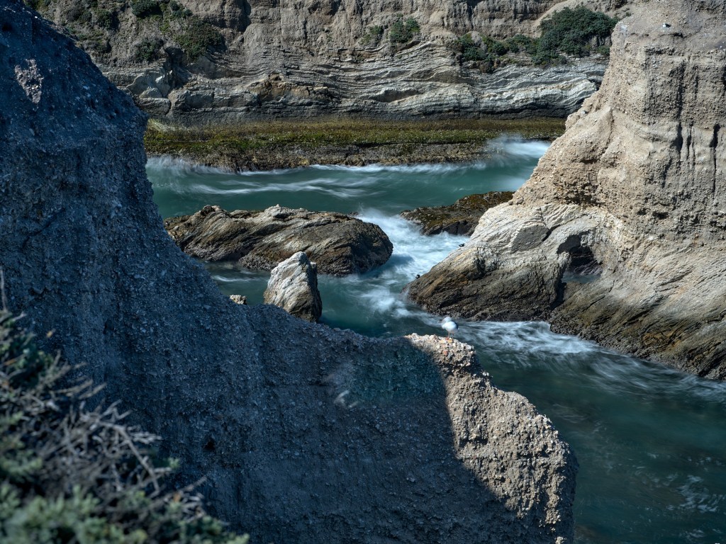 Gray sedimentary walls surround green-blue water with sunlit ledges in the background.