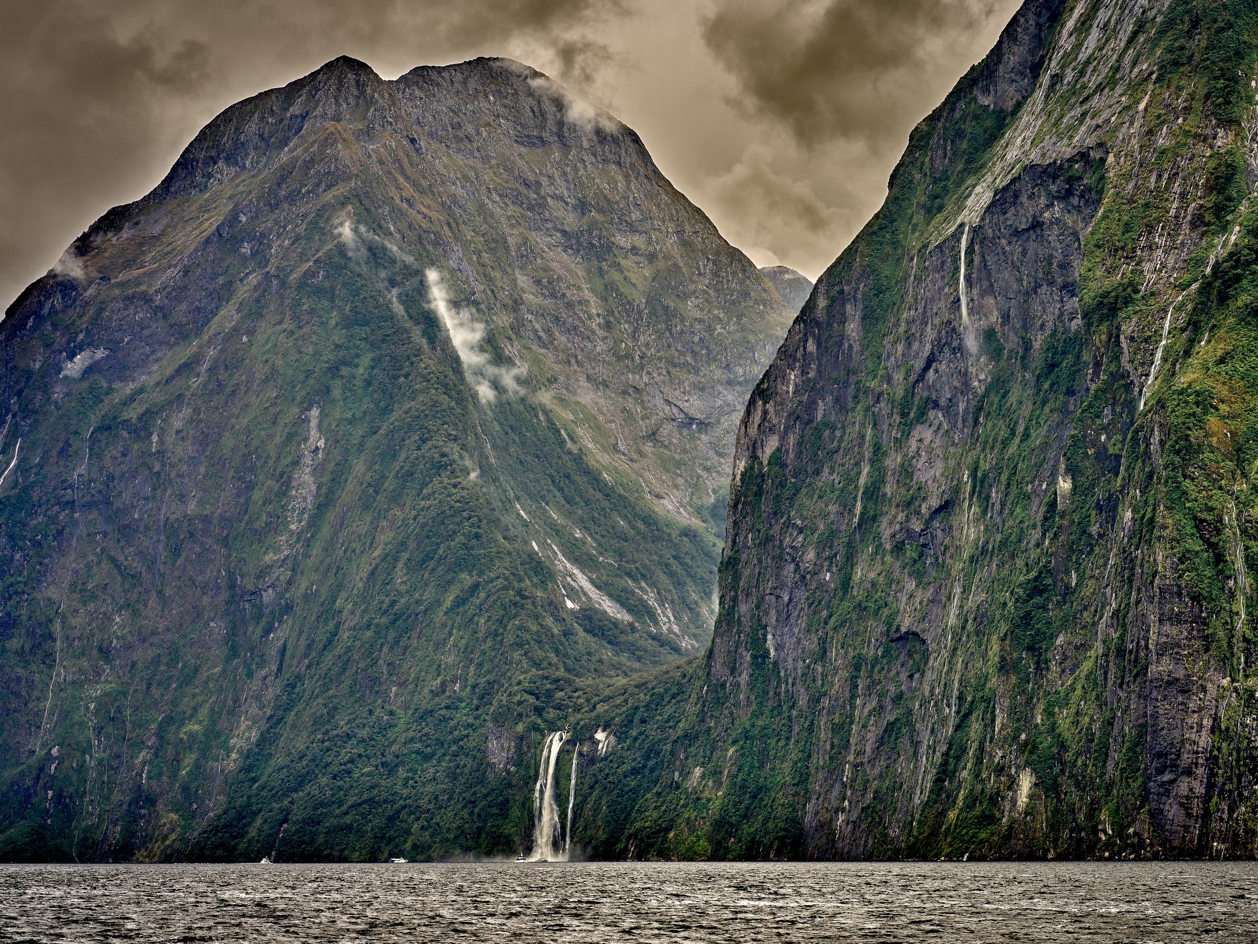 Milford Sound 10 Stirling Falls descends from a high hanging valley into Milford Sound beneath dramatic cloud-darkened cliffs.