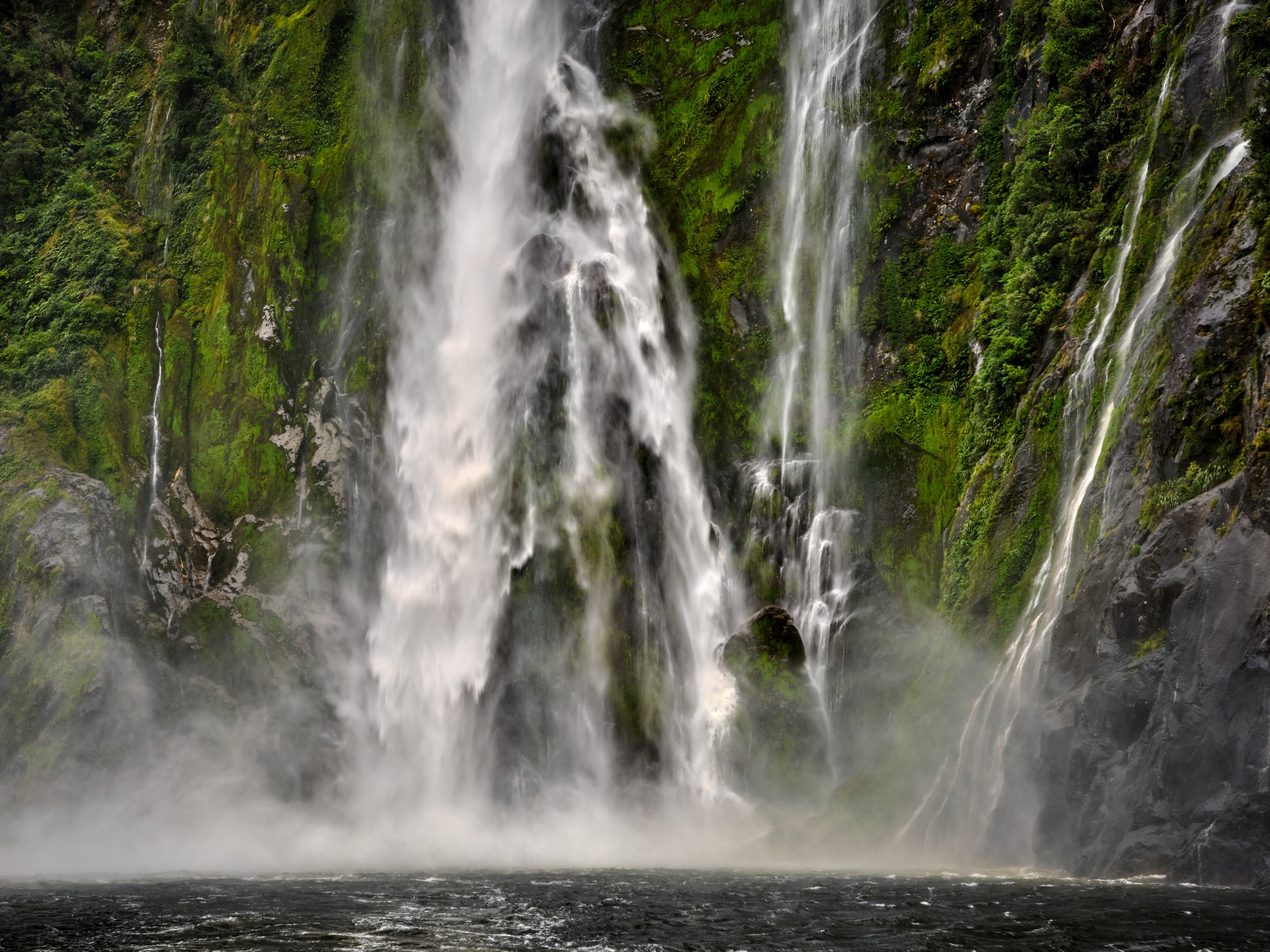 Milford Sound 5 Heavy spray erupts where Stirling Falls crashes into Milford Sound near a passing tour boat.