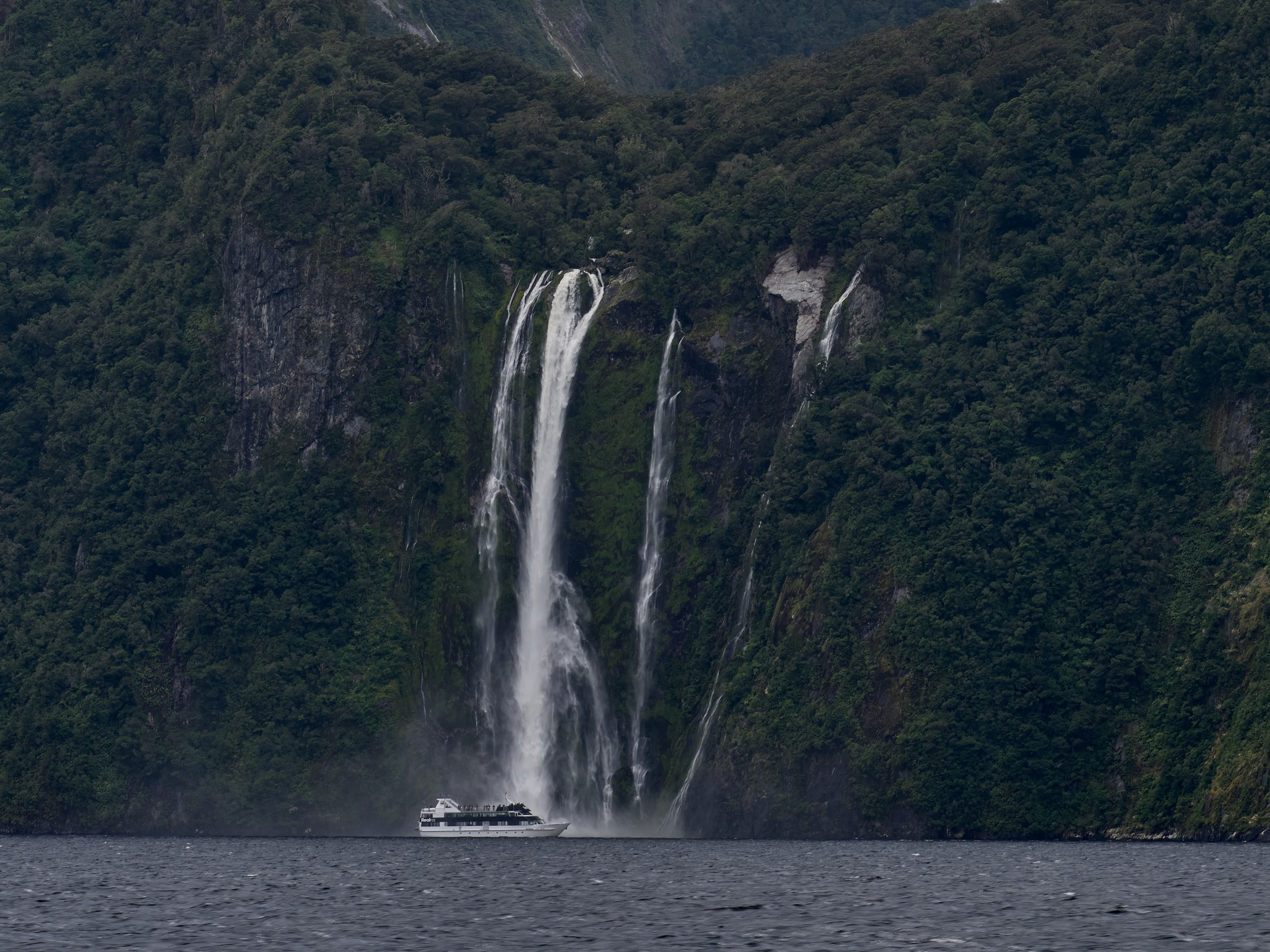 Milford Sound 17 A small tour boat passes below Stirling Falls, emphasizing the immense scale of Milford Sound?s cliffs.