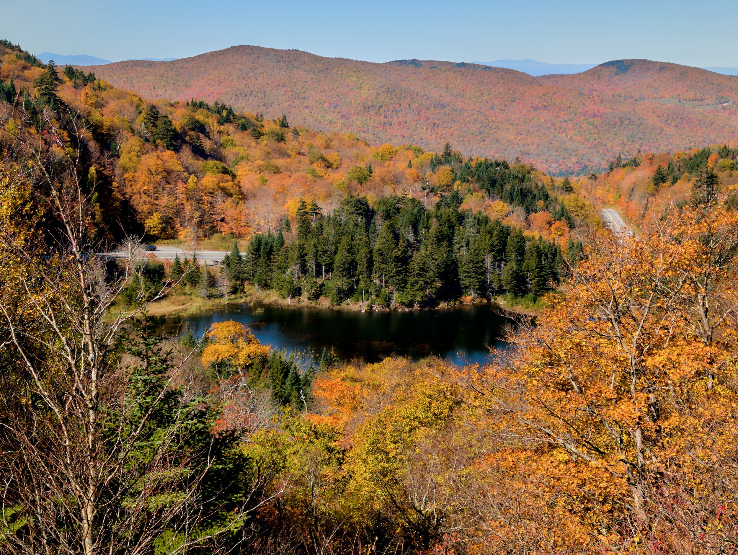 Vermont and Quebec 34 Gold and orange hardwoods frame a dark pond and layered slopes near Appalachian Gap beneath a clear blue sky.