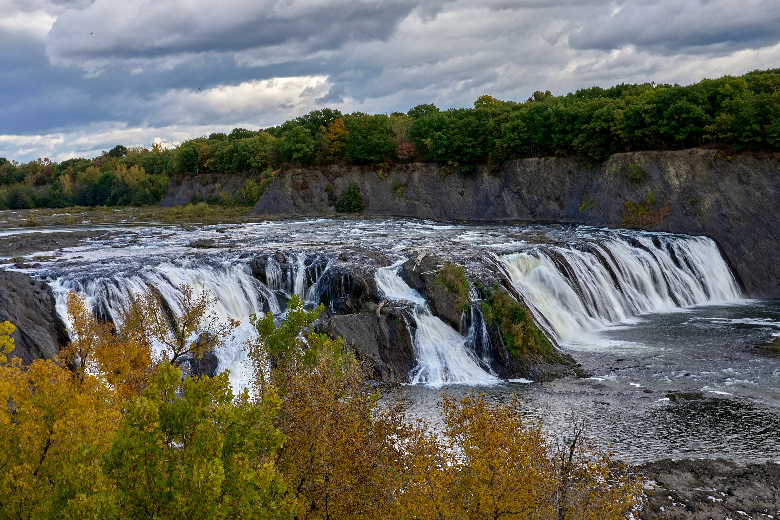 Vermont and Quebec 42 Multiple white curtains of water cross a wide rocky ledge beneath dark clouds at Cohoes Falls.