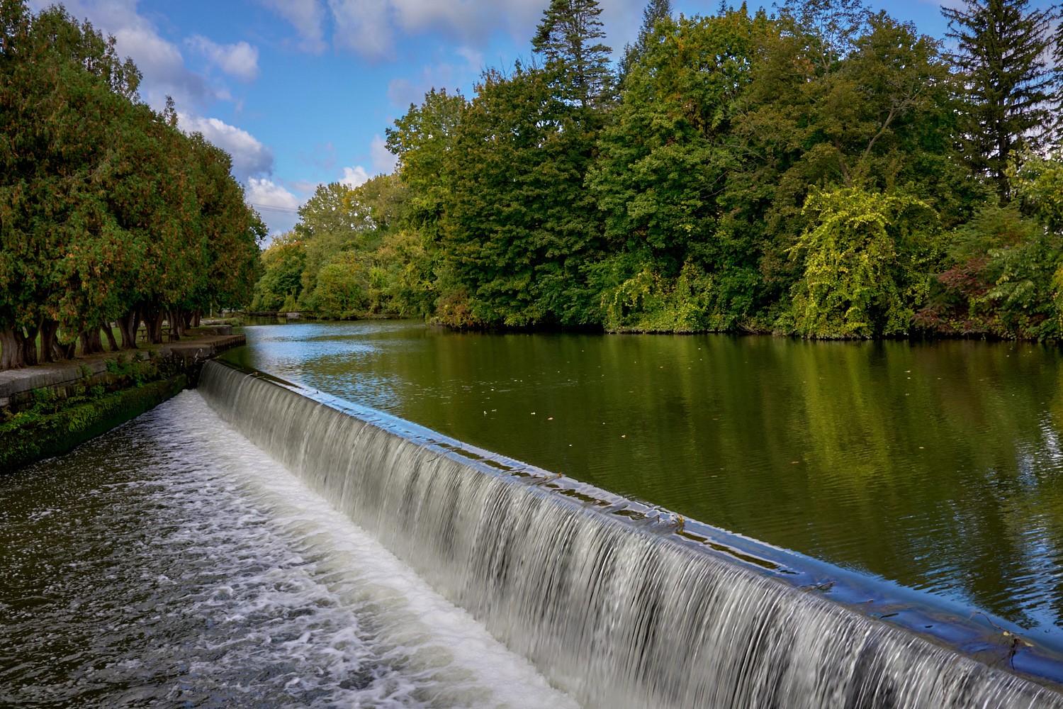 Vermont and Quebec 67 A broad curved weir spills smooth water beside a tree-lined canal at Lock E2 in Waterford.