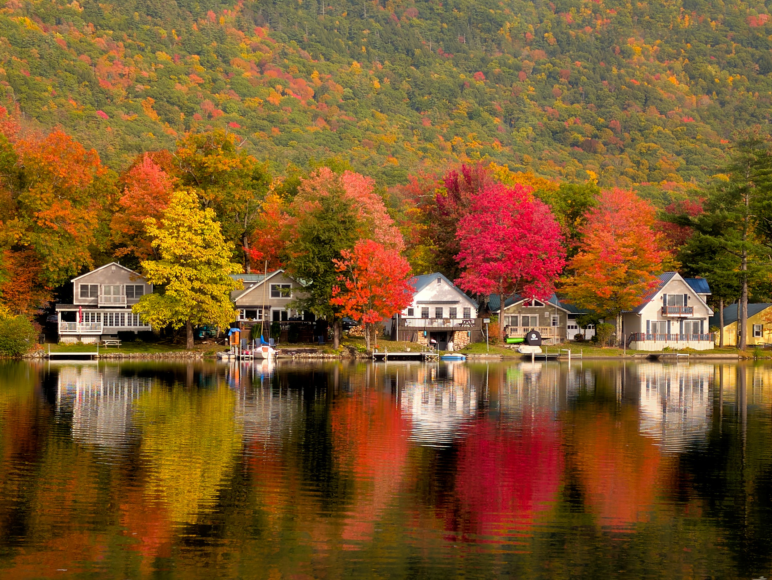 Vermont and Quebec 25 Red and orange trees mirror beside small homes on still Lake Dunmore with a forested slope behind.