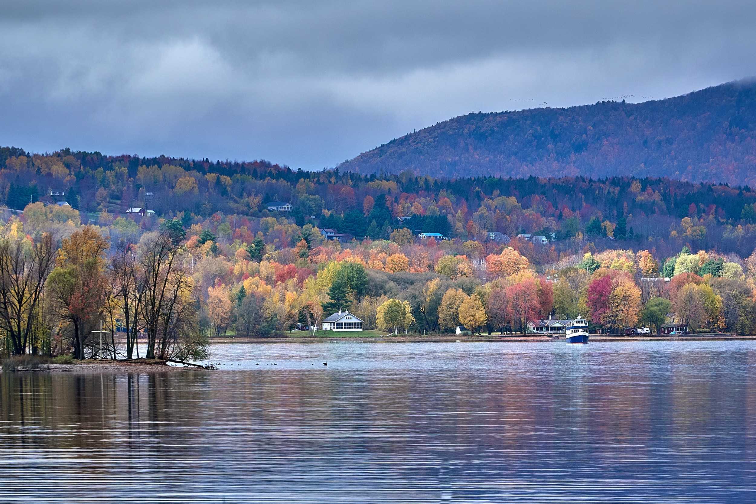 Vermont and Quebec 71 Calm Lake Memphremagog opens toward a low wooded ridge and colorful Newport shoreline beneath heavy clouds.