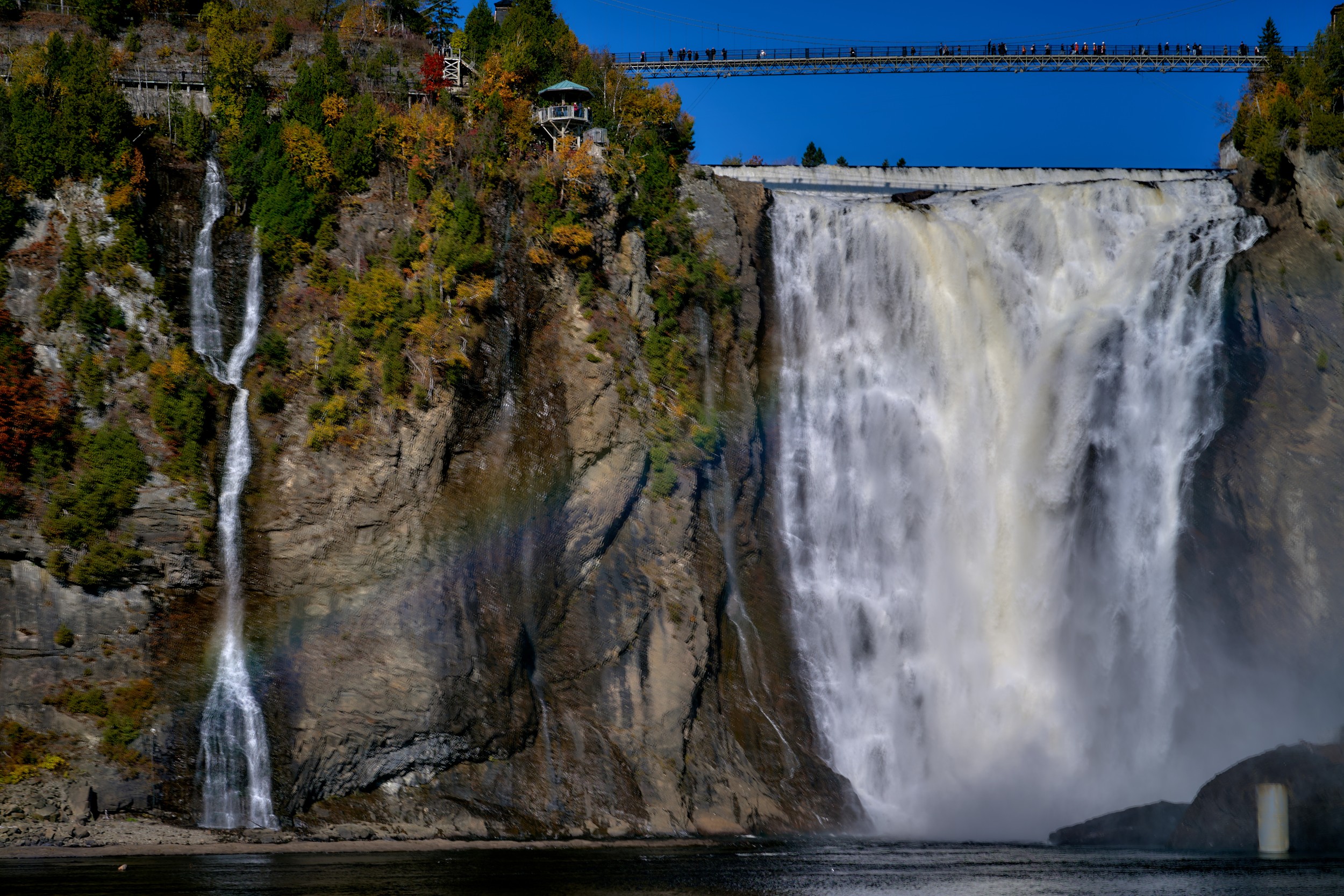 Vermont and Quebec 52 Large white curtain of water plunges into shadow beside wooded rock ledges, with a slim bridge visible high above.
