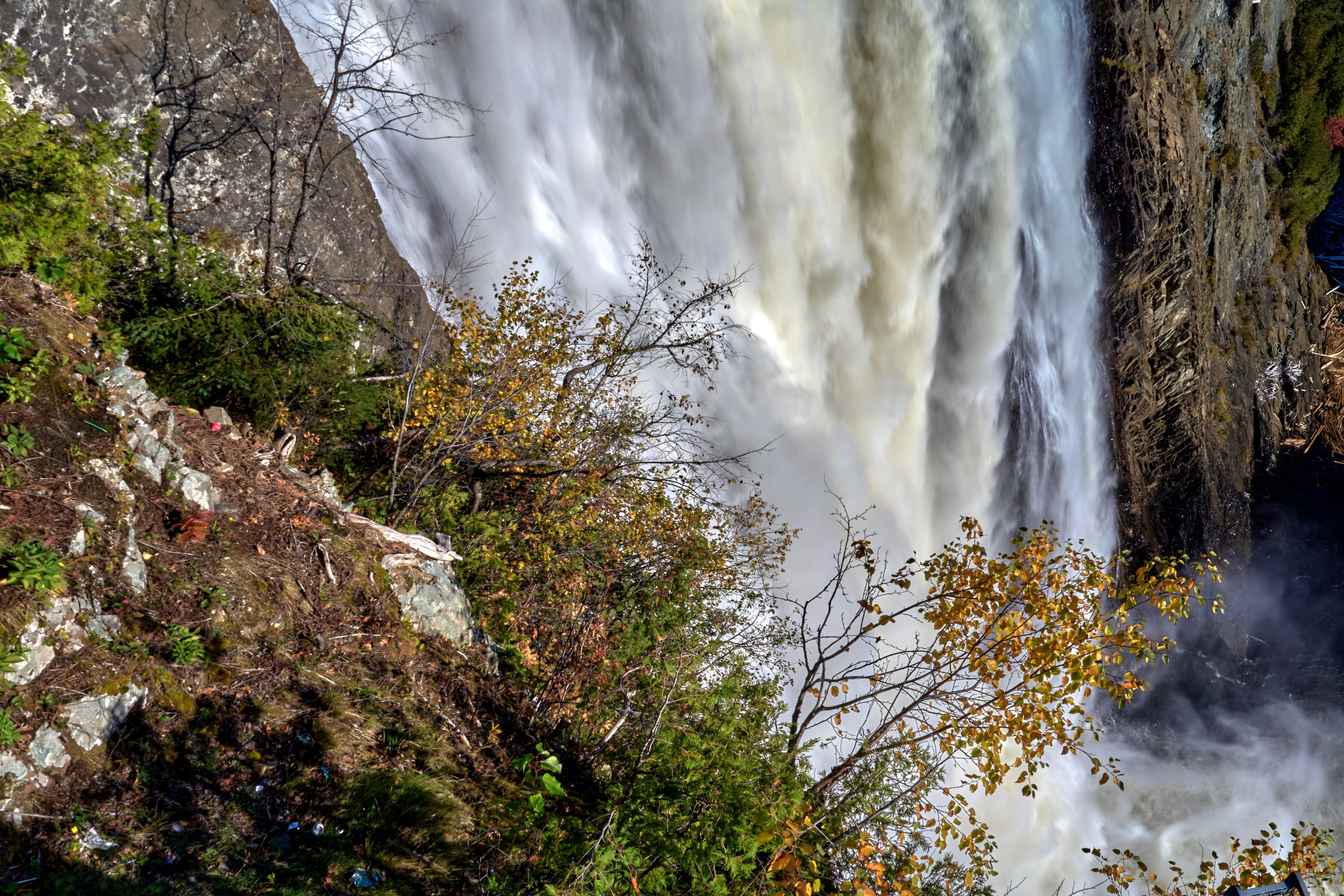 Vermont and Quebec 35 Close oblique view of a tall white waterfall with thin branches, autumn leaves and mossy rocks in the foreground.